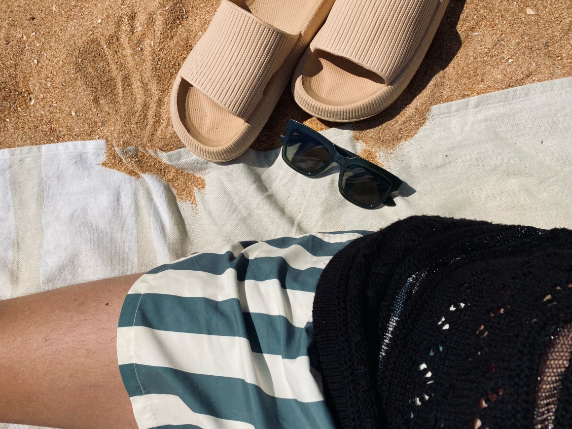 Details am Strand. Badehandtuch mit Badelatschen und Sonnenbrille. gestreifte Badehose und Shirt mit Muster
