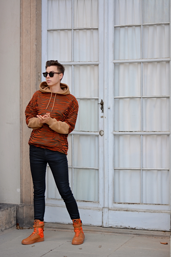 So kann man T-Shirts auch im Winter tragen. Modeblogger vor grau-weißem Hintergrund mit outfit in hellbraun/orange