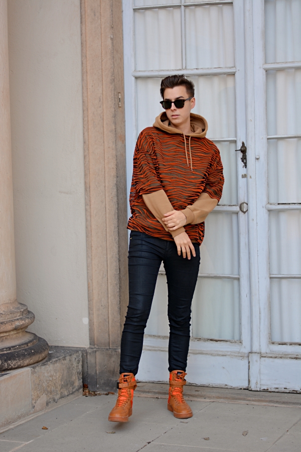 So kann man T-Shirts auch im Winter tragen. Modeblogger vor hellem Hintergrund. Outfit in hellbraun, orange und schwarz. Hände verschränkt vor Körper