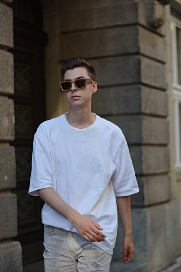 Modeblogger Pierre läuft durch Gasse. Weißes Shirt, Sonnenbrille.